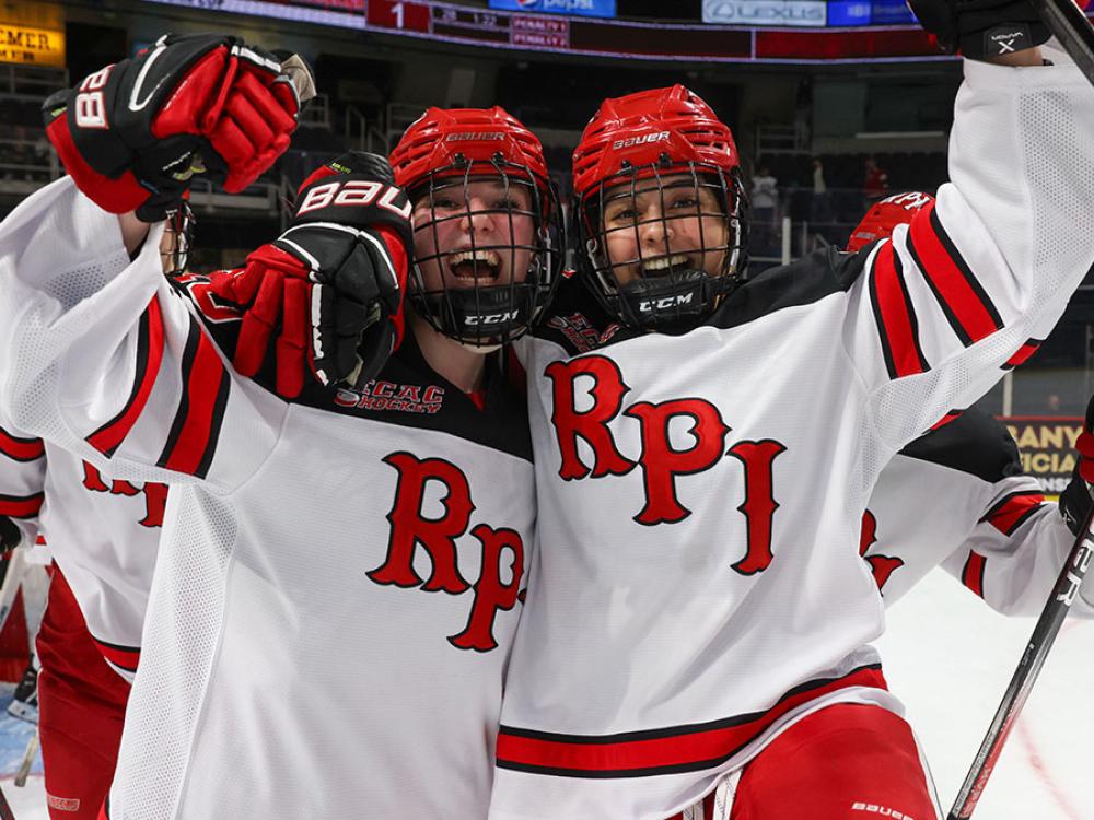 Two RPI hockey players celebrating a victory on the ice, wearing their team jerseys and helmets, their arms around each other's shoulders.