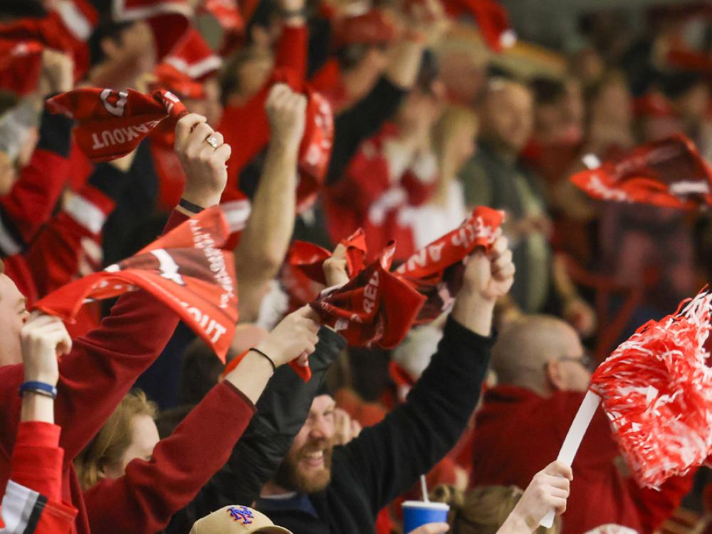 Crowd of excited spectators waving red scarves at an RPI hockey game.